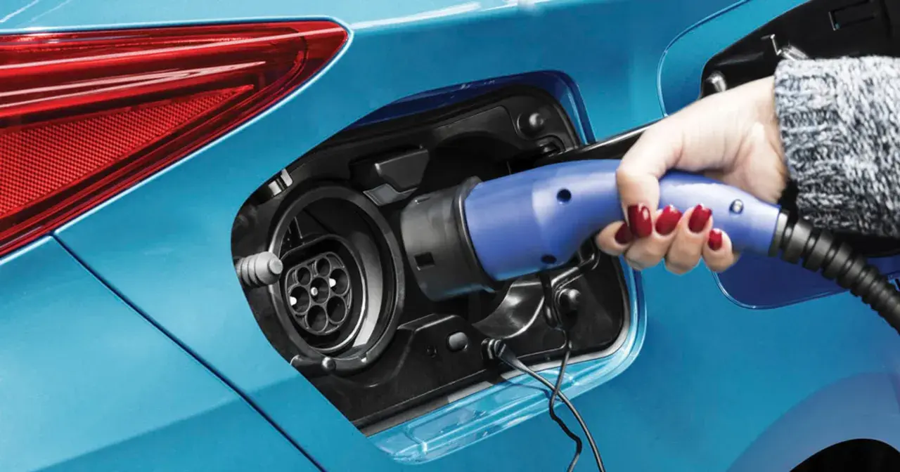 Dłoń z czerwonym lakierem na paznokciach podłącza ładowarkę do niebieskiej hybrydy plug-in.