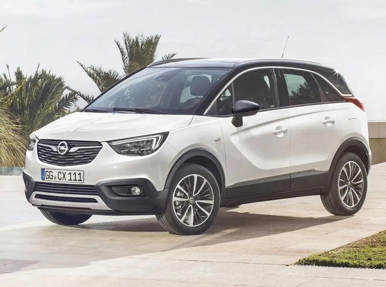 Biały Opel Crossland z czarnym dachem, zaparkowany na tarasie z palmami w tle. Wiele pozytywnych opinii o tym modelu.
