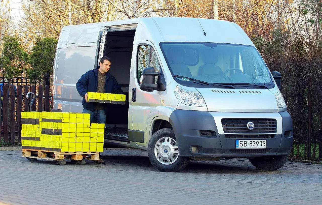Mężczyzna rozładowuje żółte paczki z furgonetki Fiat Ducato 2.3.