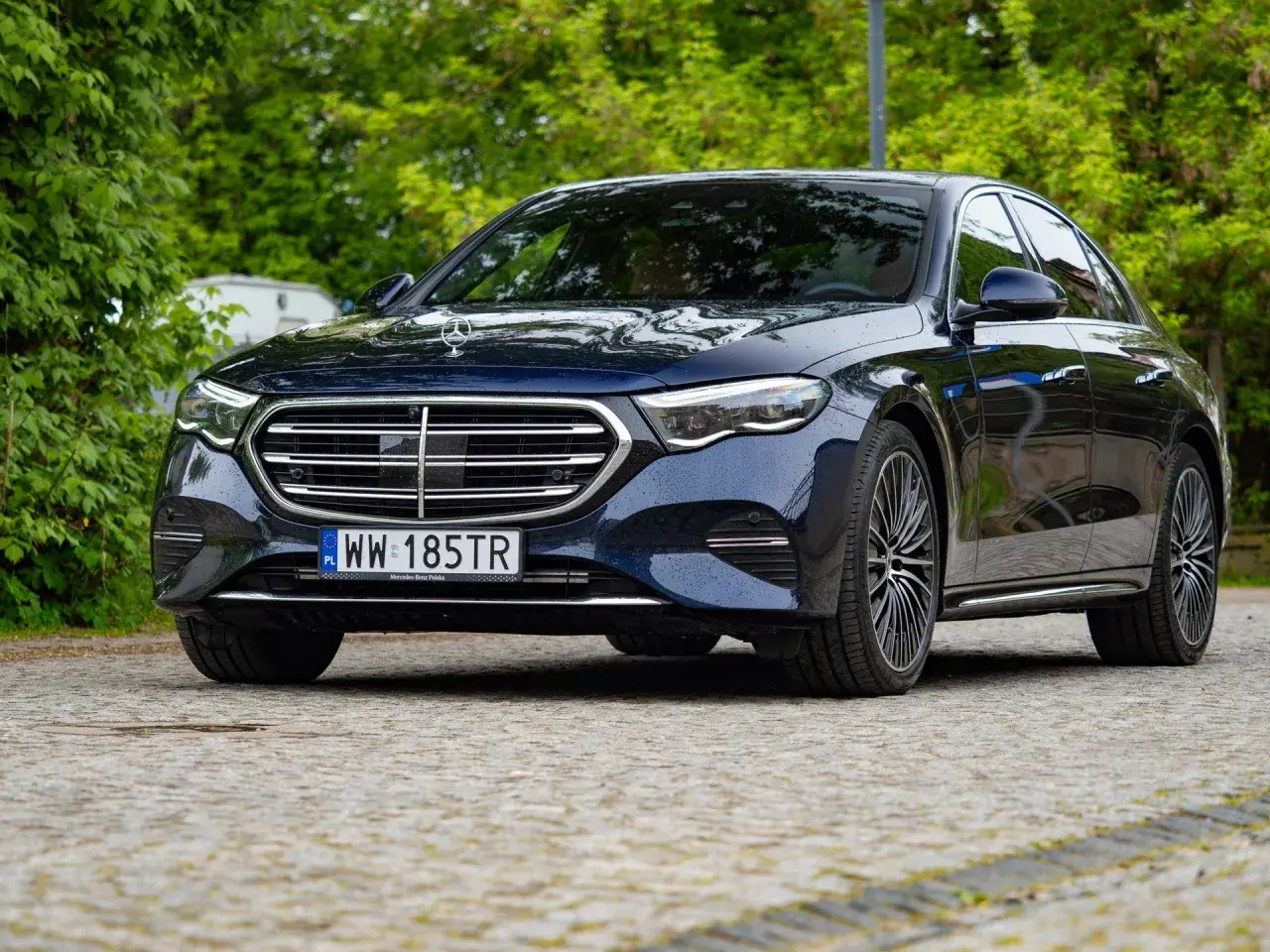 Elegancki, ciemnogranatowy Mercedes e300 lśni po deszczu na tle zieleni.