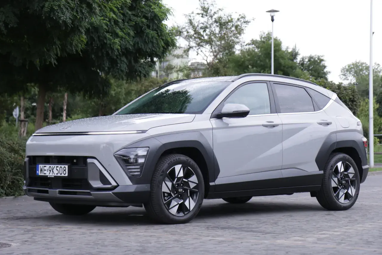 Nowe Hyundai Kona opinie: szary SUV z nowoczesnym designem, zaparkowany na bruku, otoczony zielenią.