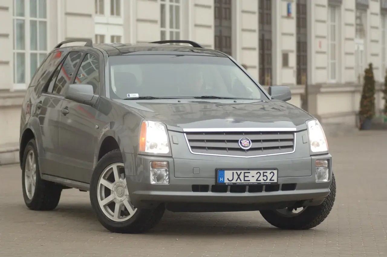 Szary Cadillac SRX z tablicą rejestracyjną JXE-252 zaparkowany przed budynkiem.