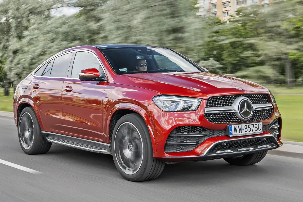 Czerwony Mercedes-Benz GLE Coupe, model gle amg, pędzi po drodze, za kierownicą siedzi kierowca w okularach.