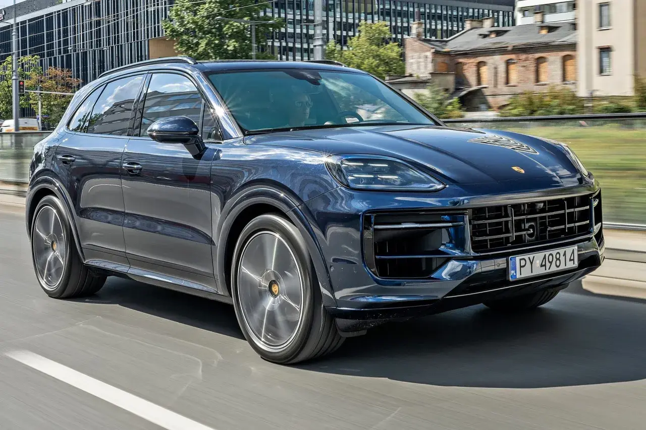 Ciemnoniebieski Porsche Cayenne w ruchu miejskim. Sprawdź aktualną porsche cayenne cena, aby poznać jego atrakcyjność.