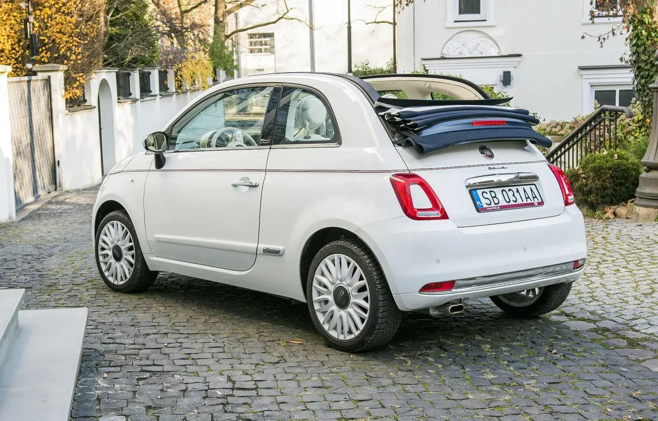 Biały fiat 500c cabrio z otwartym dachem stoi na brukowanej uliczce.