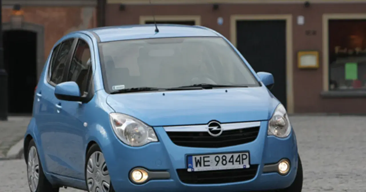 Niebieski Opel Agila 1.2 na brukowanej ulicy przed budynkiem.