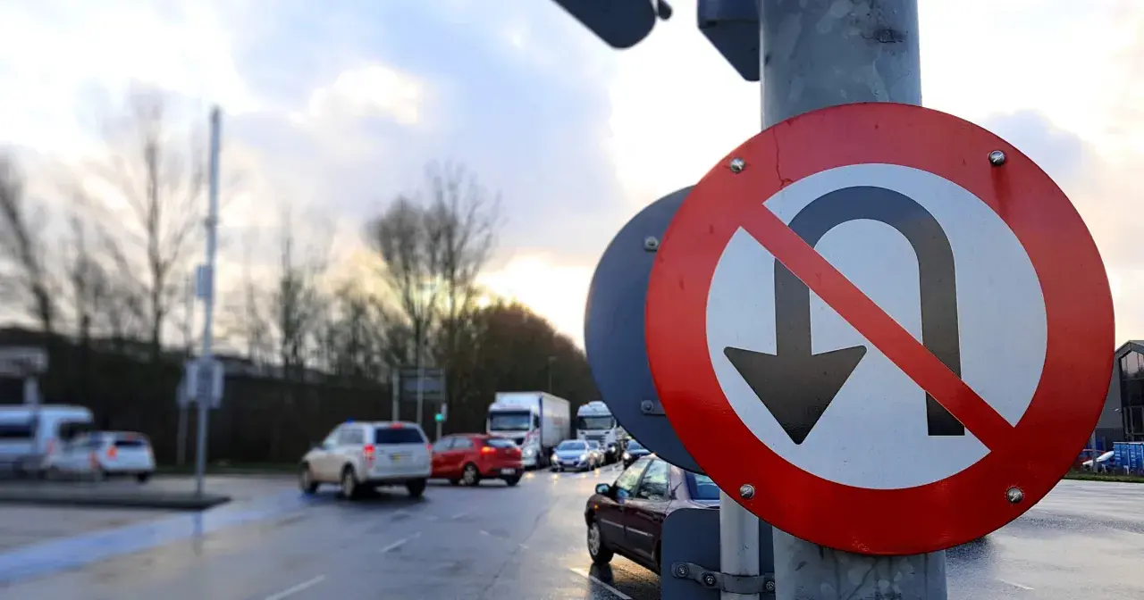 Znak zakazu zawracania na skrzyżowaniu. Samochody stoją w deszczu, czekając na zielone światło.