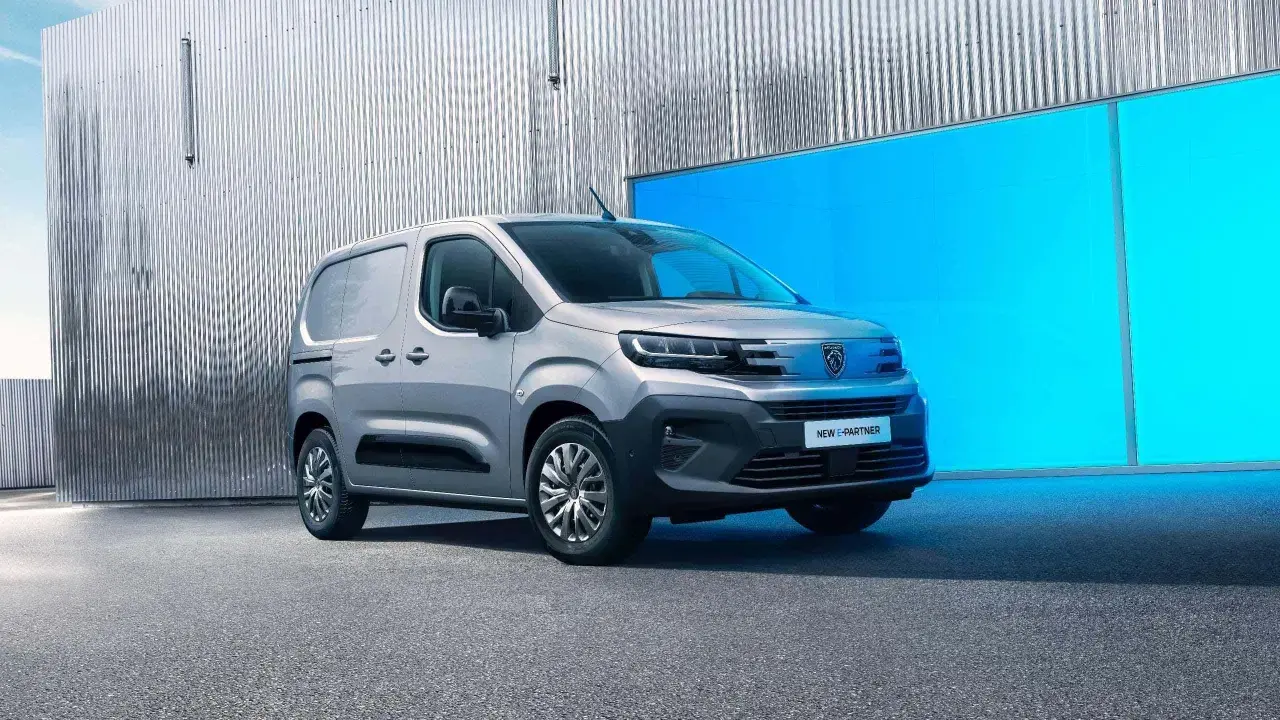 Nowy Peugeot e-Partner, srebrny van, stoi przed błyszczącą, falistą ścianą i jaskrawoniebieskim panelem.