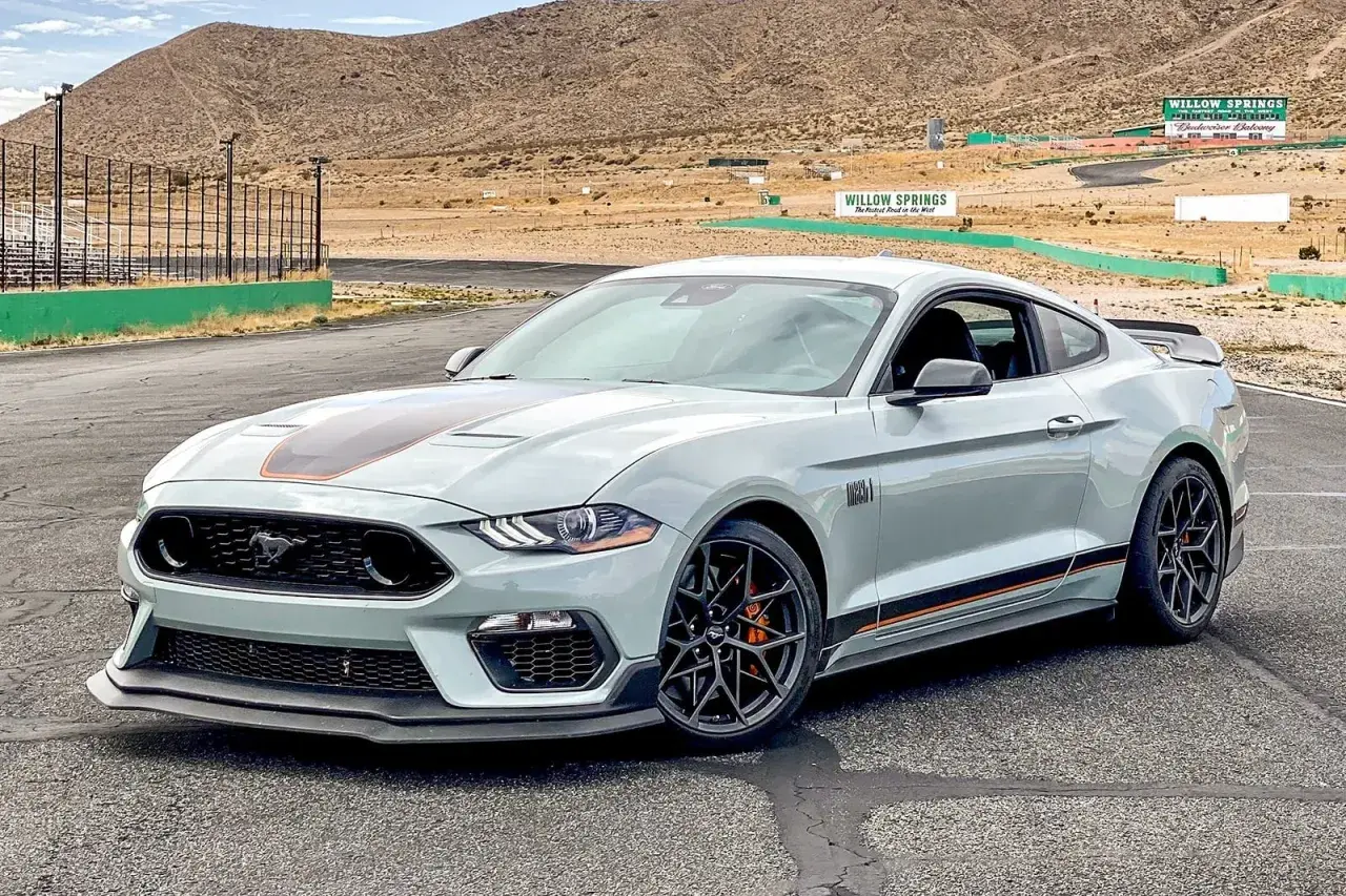 Jasnoszary Mustang GT 5.0 z pomarańczowymi akcentami na torze wyścigowym Willow Springs.