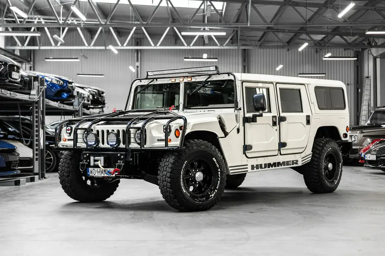 Biały Hummer H1 z potężnymi oponami i dodatkowym oświetleniem na dachu, gotowy na każdą przygodę.