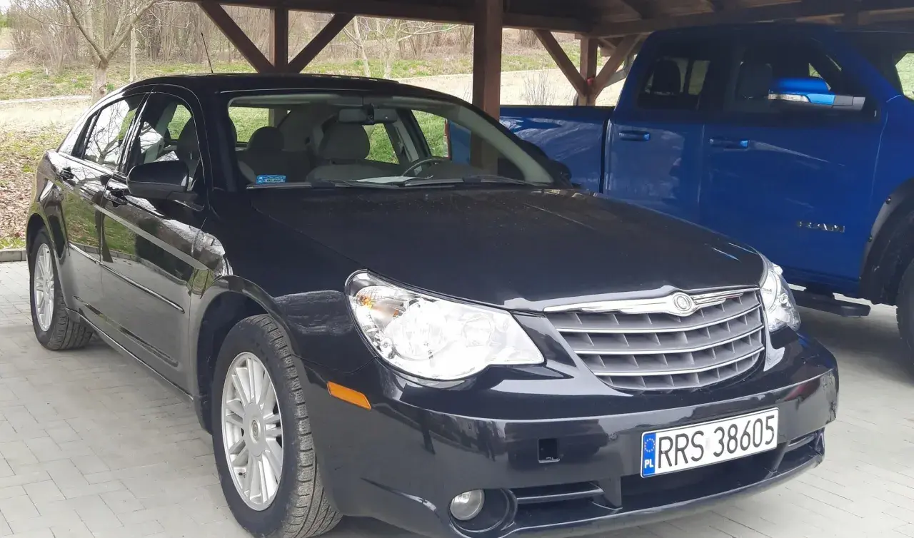 Czarny Chrysler Sebring pod wiatą, obok niebieski pickup.