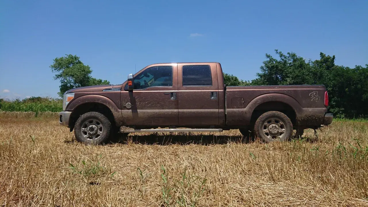 Brązowy Ford F250, ubrudzony ziemią, stoi na polu z suchą trawą.