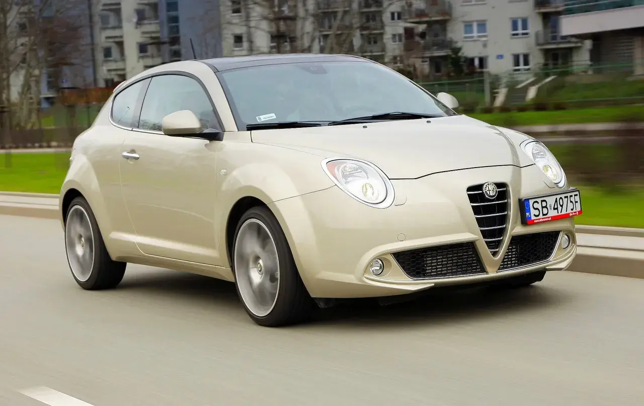 Złoty Alfa Romeo MiTo w ruchu miejskim. Wiele osób chwali ten model za wygląd, co potwierdzają alfa romeo mito opinie.