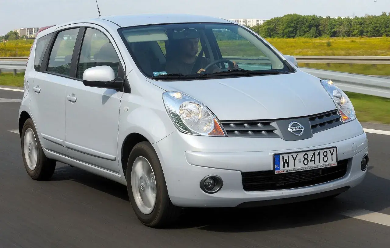 Srebrny Nissan Note na drodze. Kierowca w czapce prowadzi auto. Wiele osób szuka nissan note opinie przed zakupem.