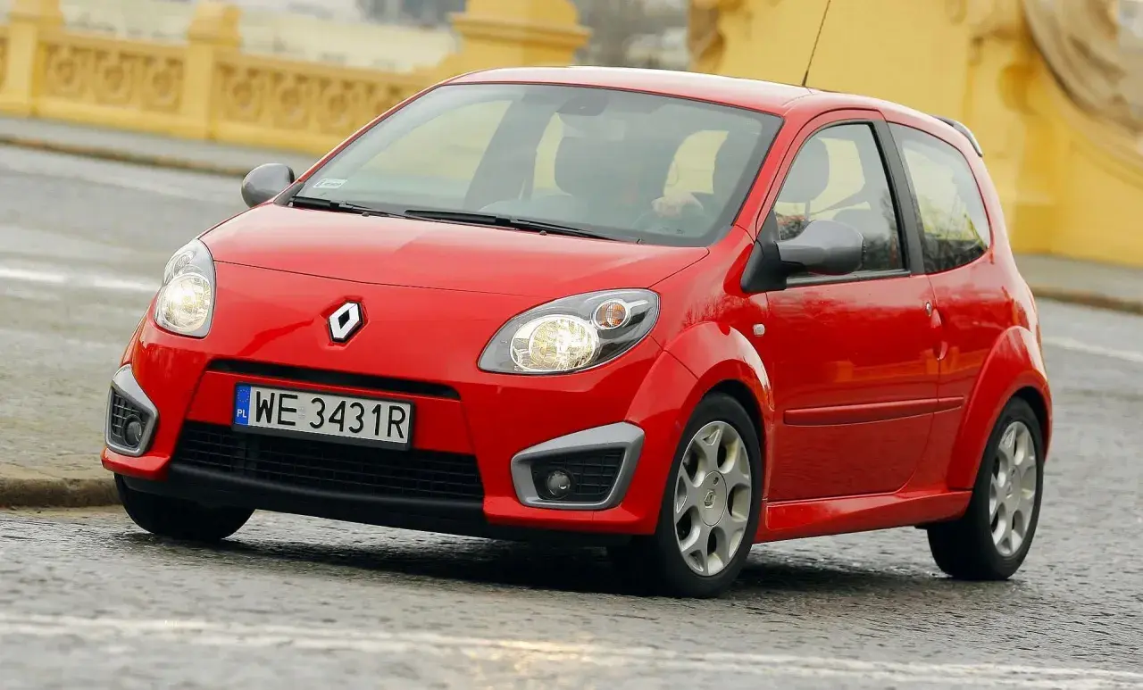 Czerwone Twingo RS na mokrej nawierzchni, z widocznym kierowcą za kierownicą.