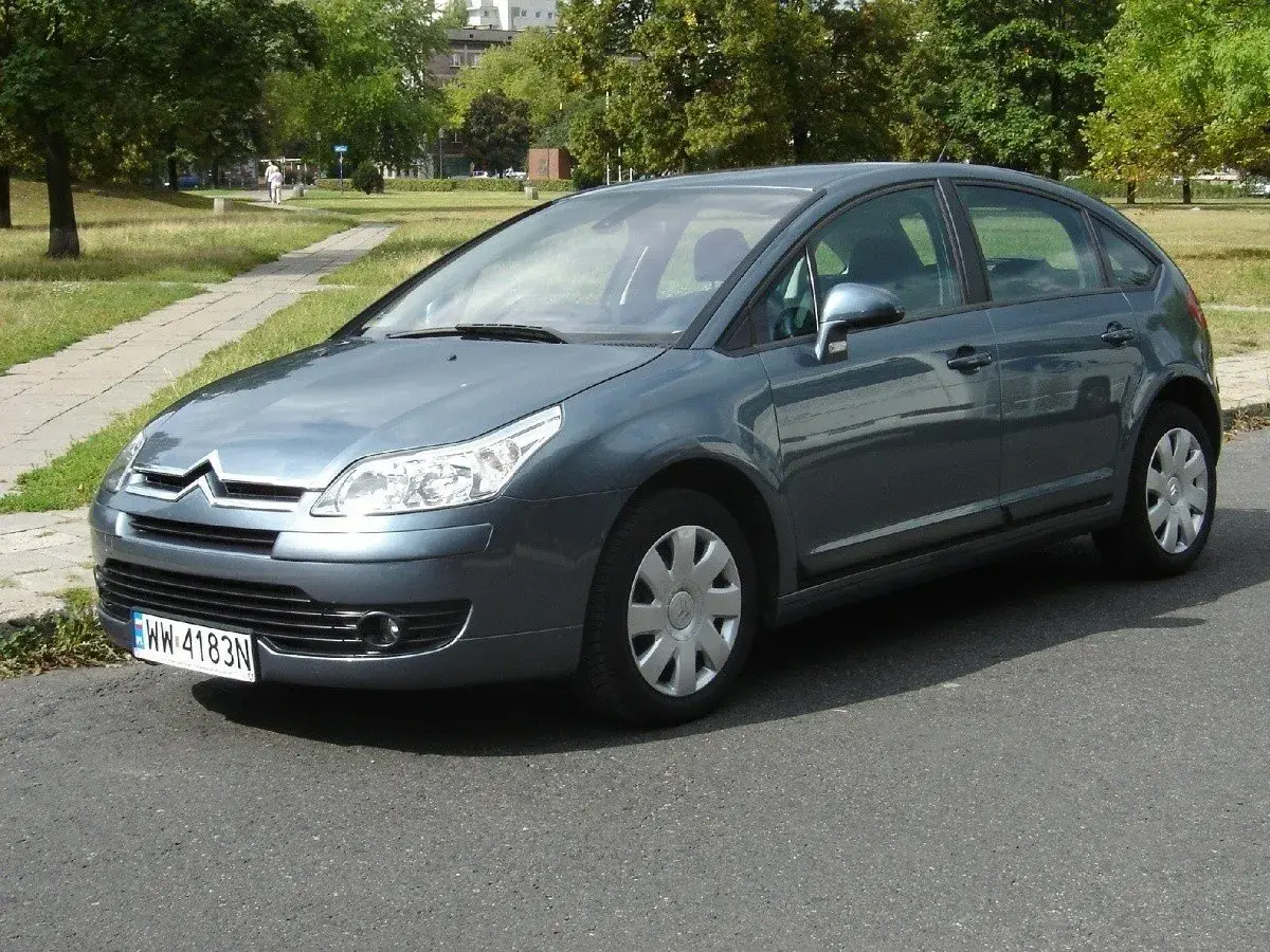 Szary Citroen C4 1.6 HDI zaparkowany przy chodniku w parku.
