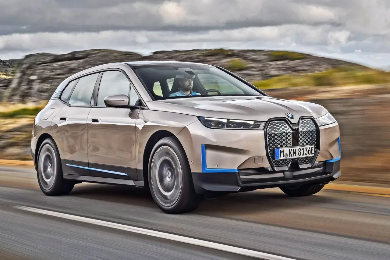 Elegancki suv BMW iX jedzie drogą wśród skalistych wzgórz.