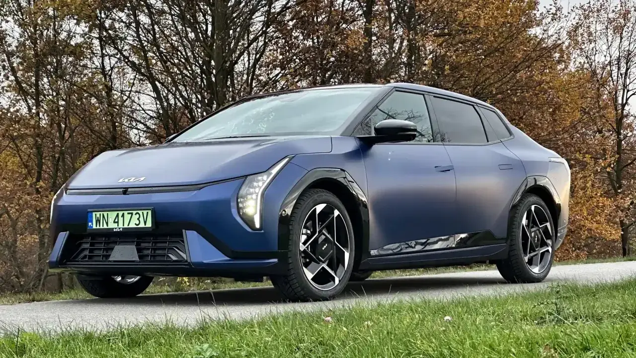 Niebieski kia sedan z matowym wykończeniem, zaparkowany na tle jesiennych drzew.