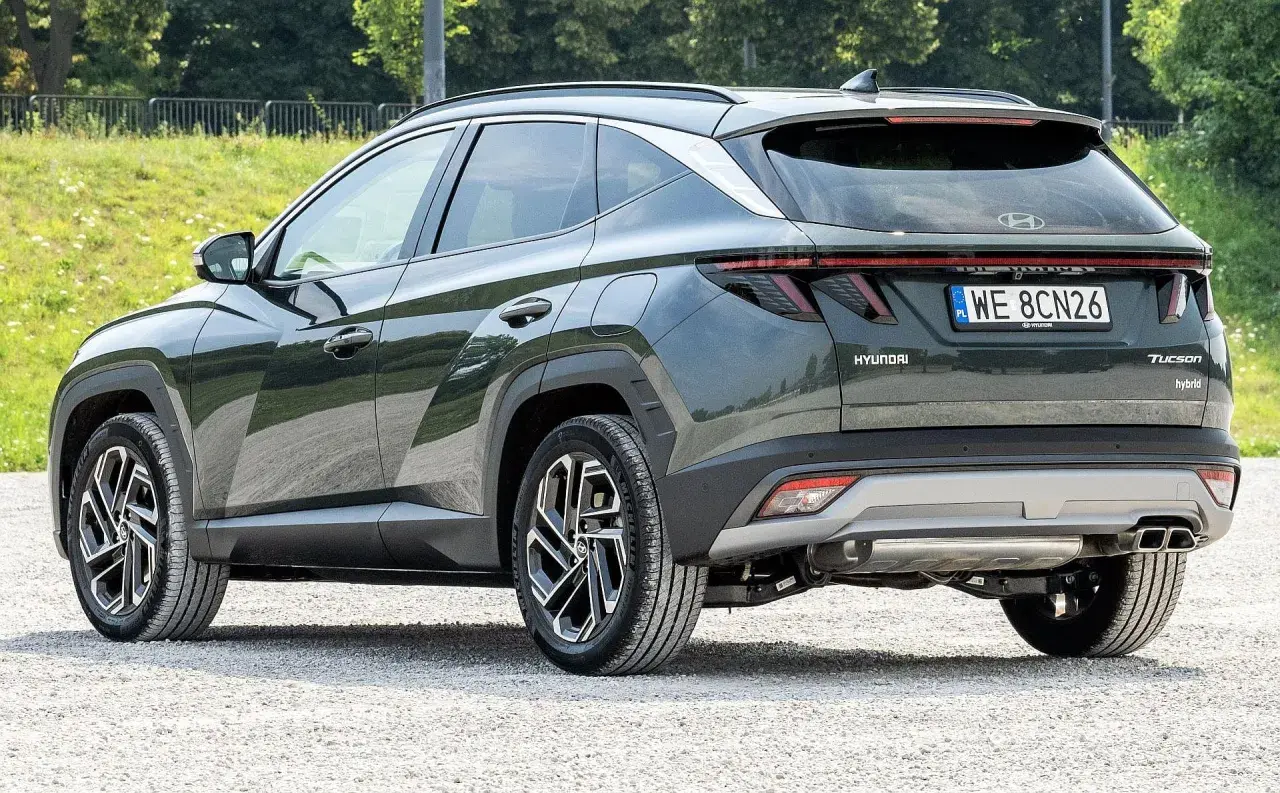 Tylna część ciemnozielonego Hyundaia Tucsona hybrydowego na żwirowej drodze. Wiele osób szuka hyundai tucson opinie przed zakupem.