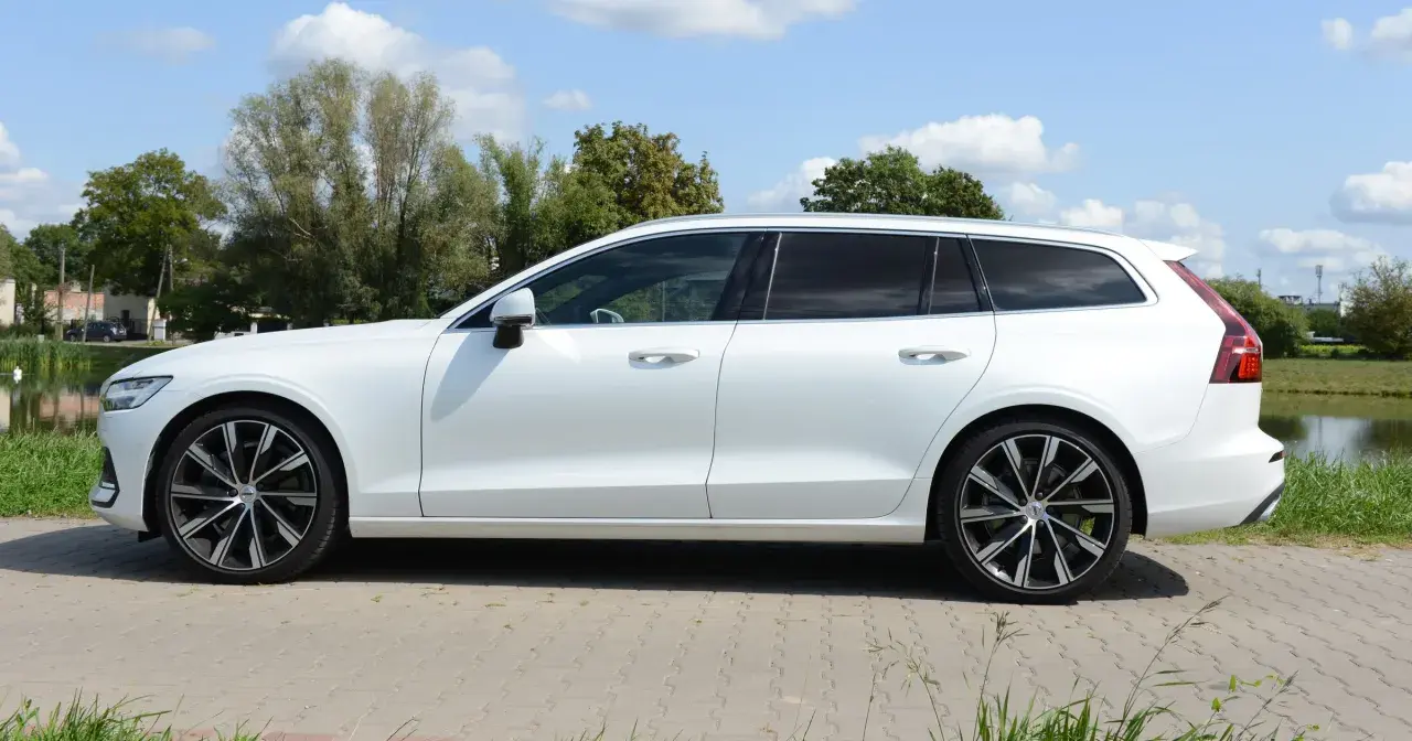 Białe Volvo T6 kombi stoi na tle zieleni i błękitnego nieba.