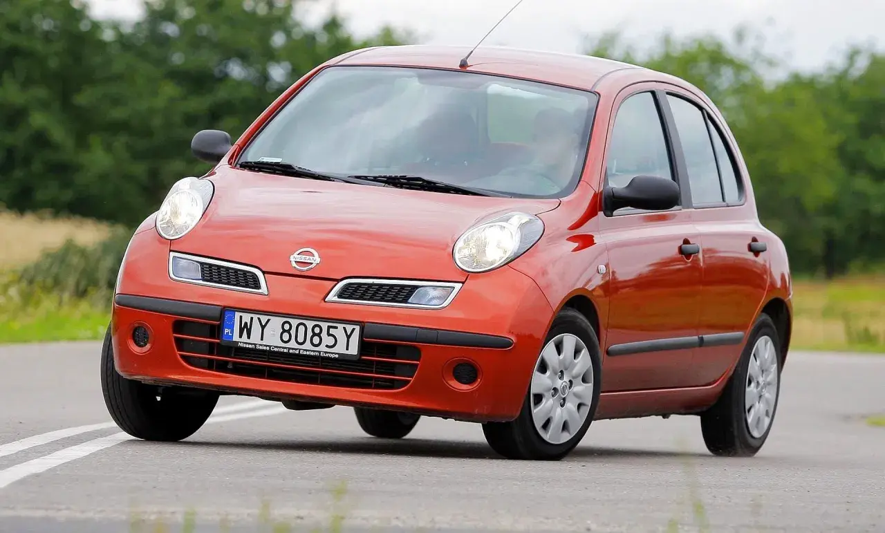 Pomarańczowy Nissan March z tablicą rejestracyjną WY 8085Y jedzie po drodze wśród zieleni.