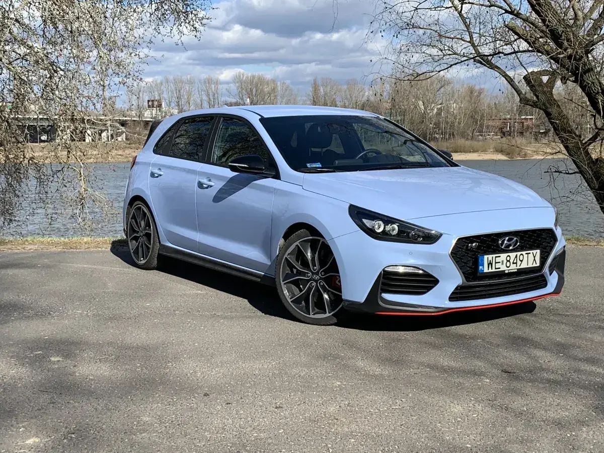 Niebieski Hyundai i30 N z czerwonymi akcentami stoi nad jeziorem, gotowy na wiosenną przejażdżkę.