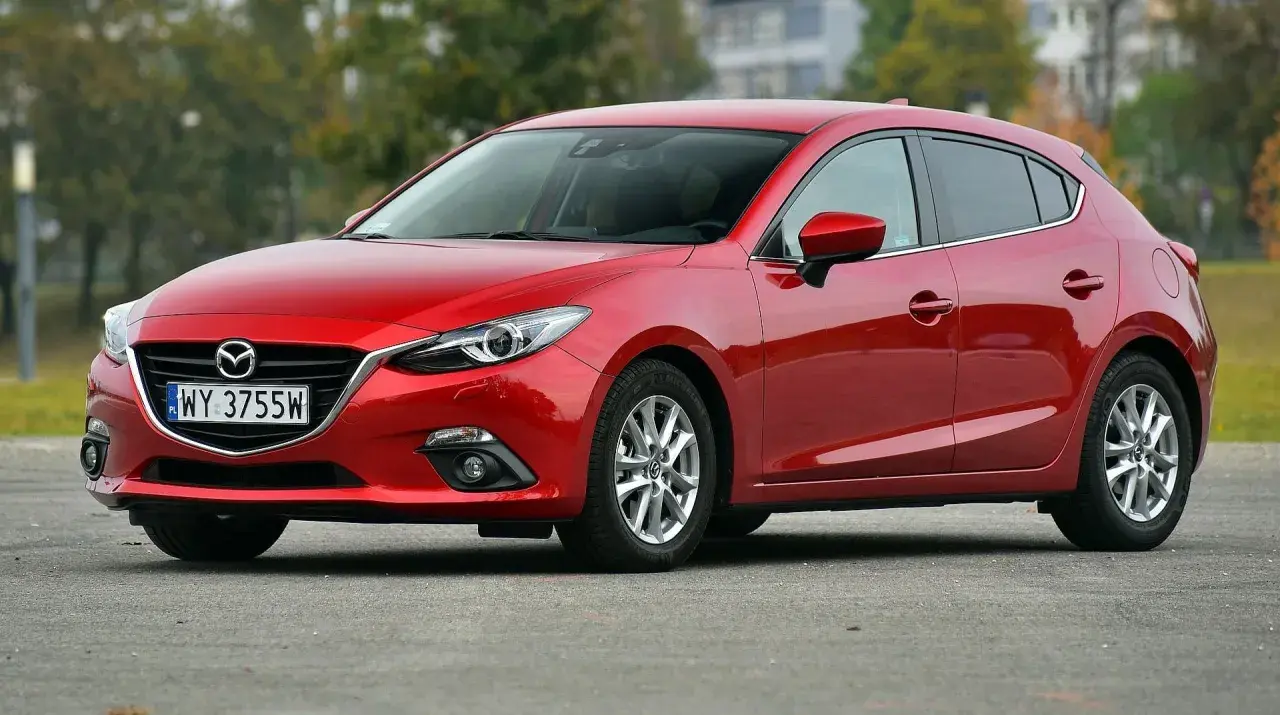 Czerwona Mazda 3 2015 na parkingu, z widocznym numerem rejestracyjnym WY 3755W.