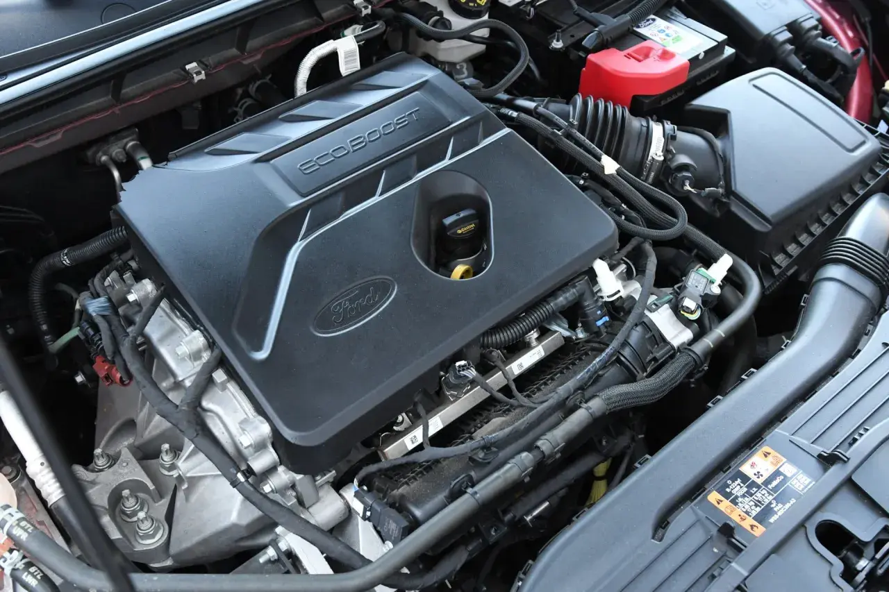 Silnik EcoBoost w Fordzie Escape 2020. Widoczna pokrywa silnika z logo Ford i napisem EcoBoost, akumulator i elementy układu dolotowego.