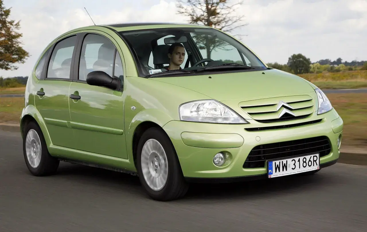 Zielony Citroen C3 z 2003 roku jedzie po drodze, za kierownicą młody mężczyzna.