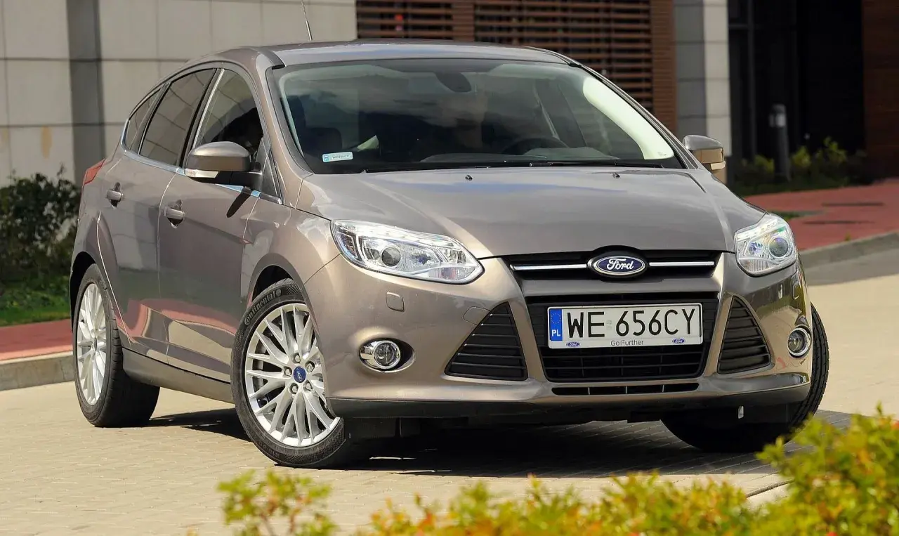 Brązowy Ford Focus MK3, często chwalony w opiniach, prezentuje się elegancko na tle nowoczesnego budynku.