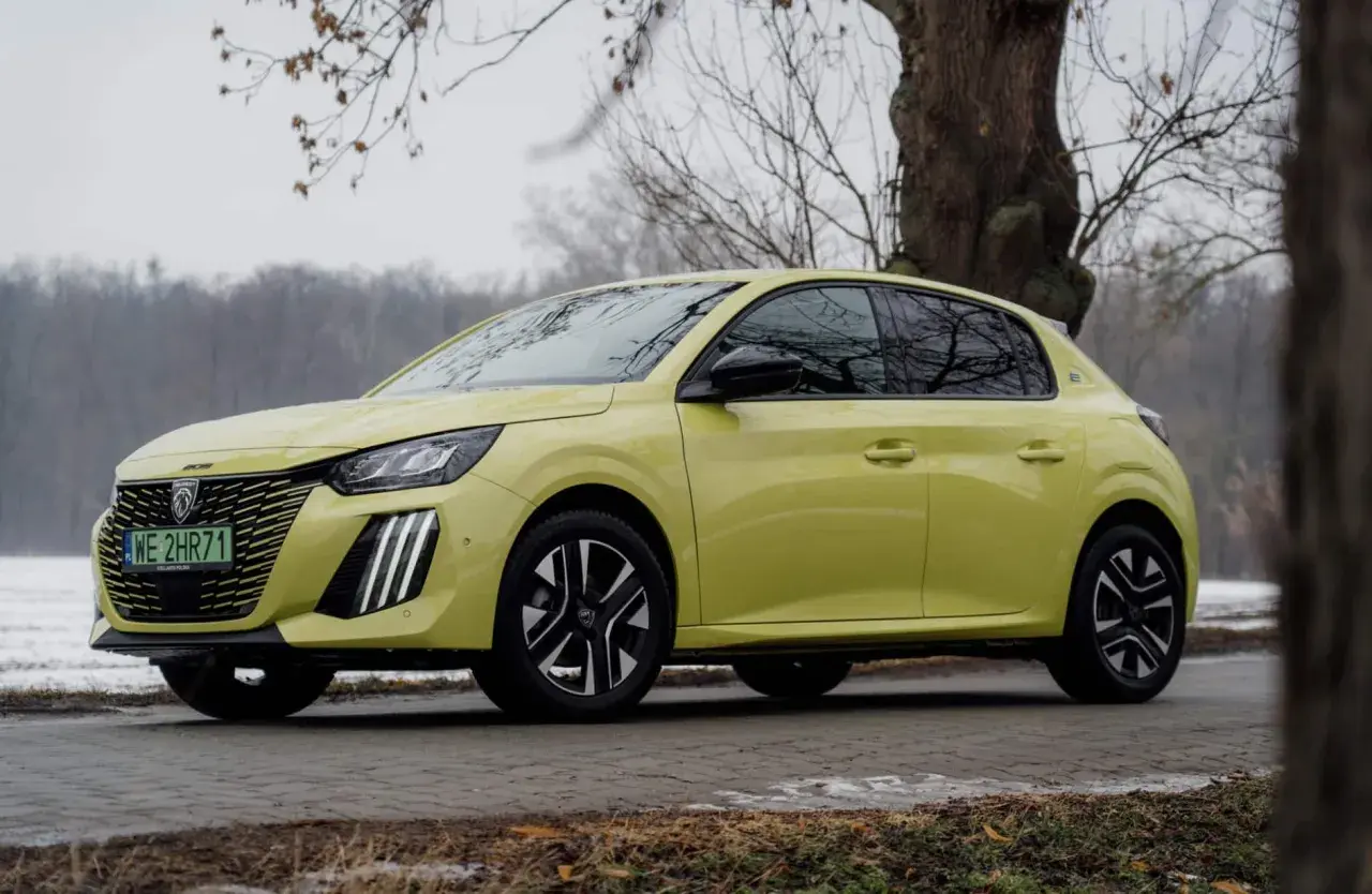 Żółty Peugeot e-208 stoi na tle drzew i zimowego krajobrazu.