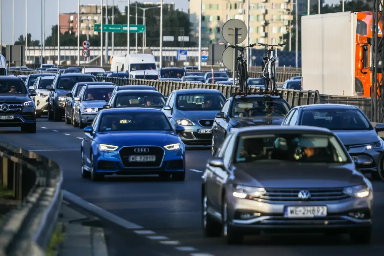 Korek uliczny, różne rodzaje samochodów osobowych i dostawczych, w tym luksusowe marki i auta z rowerami na dachu.