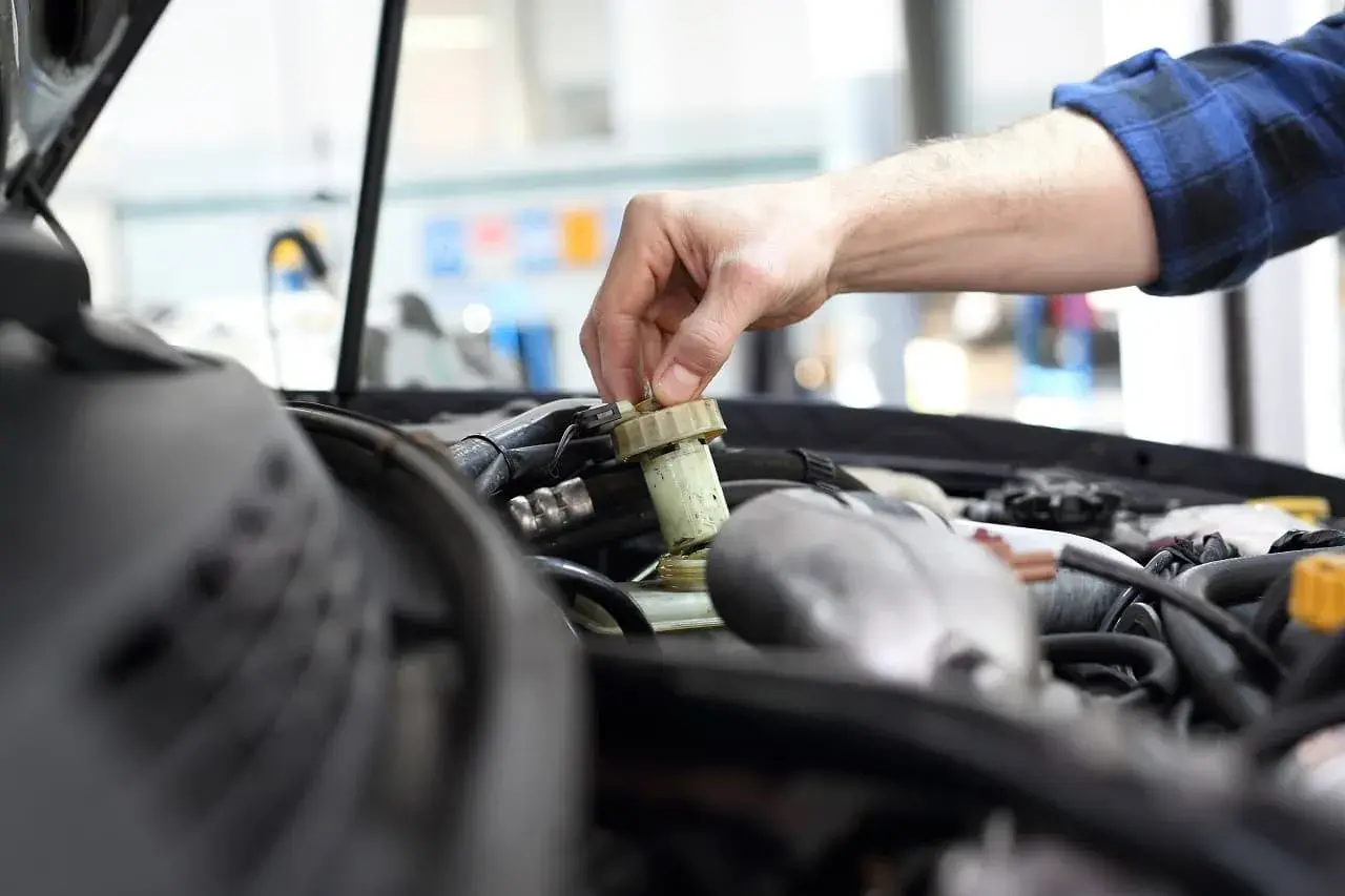 Ręka mechanika dokręca korek zbiorniczka płynu hamulcowego. Zapobiega to mandatom, od kiedy kara za spóźniony przegląd jest surowa.