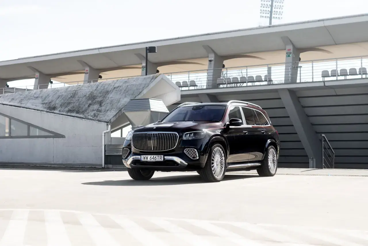 Elegancki, czarny Mercedes GLS Maybach z chromowanymi detalami i charakterystycznym grillem, zaparkowany na tle nowoczesnej architektury stadionu.