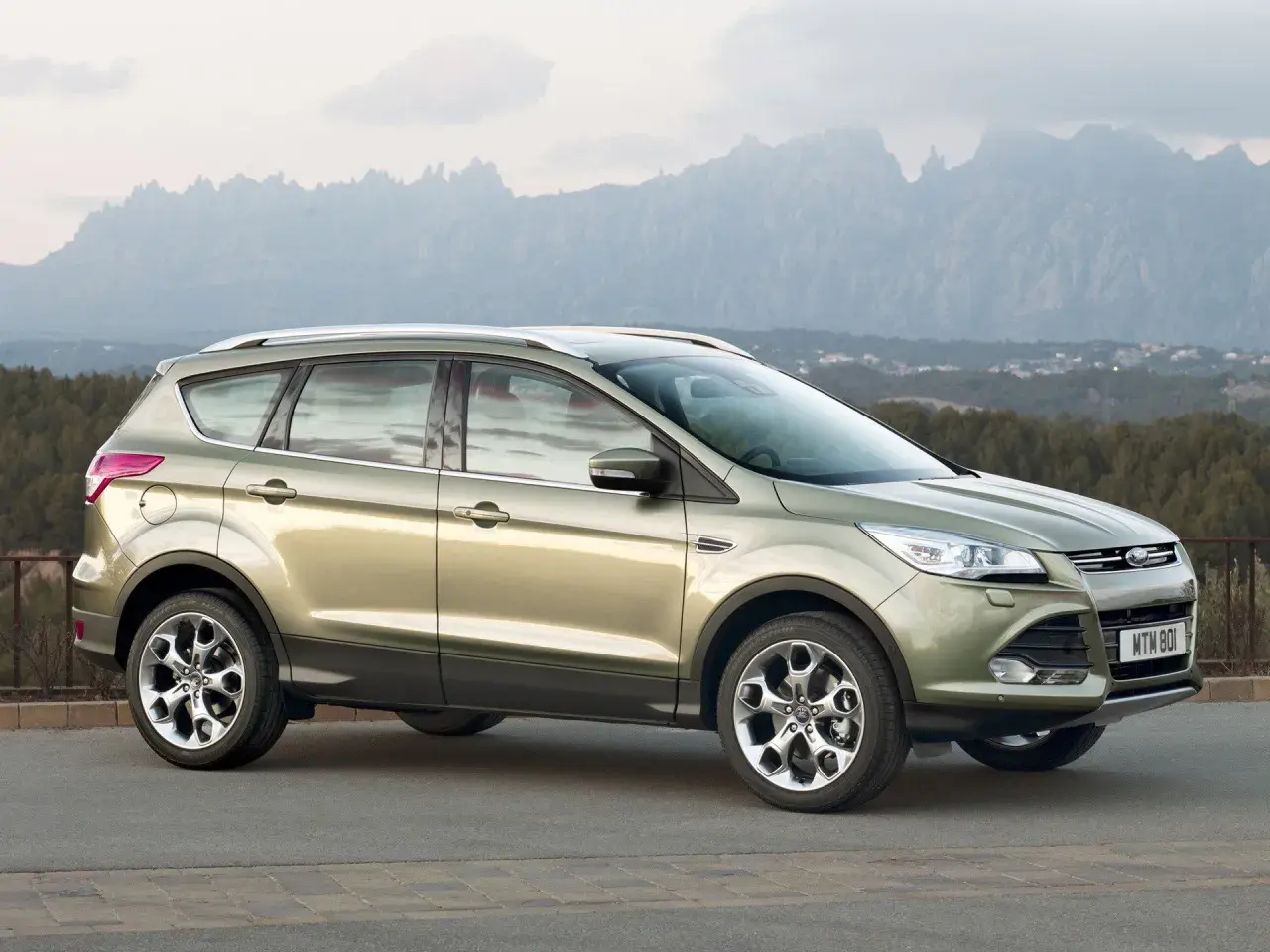 Złoty Ford Kuga na tle górskich krajobrazów. Wiele osób chwali ten model, a jego opinie są pozytywne.