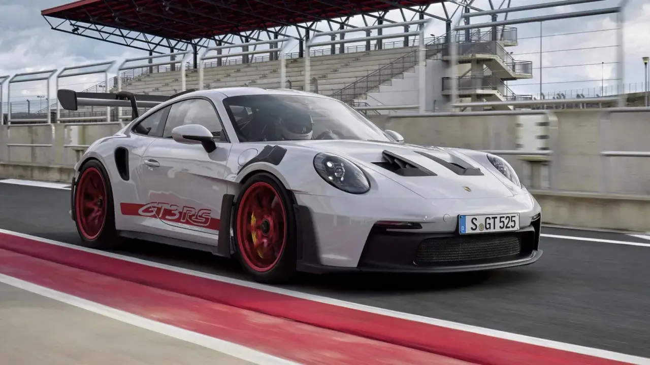 Biały Porsche 992 GT3 RS z czerwonymi akcentami i felgami pędzi po torze wyścigowym.
