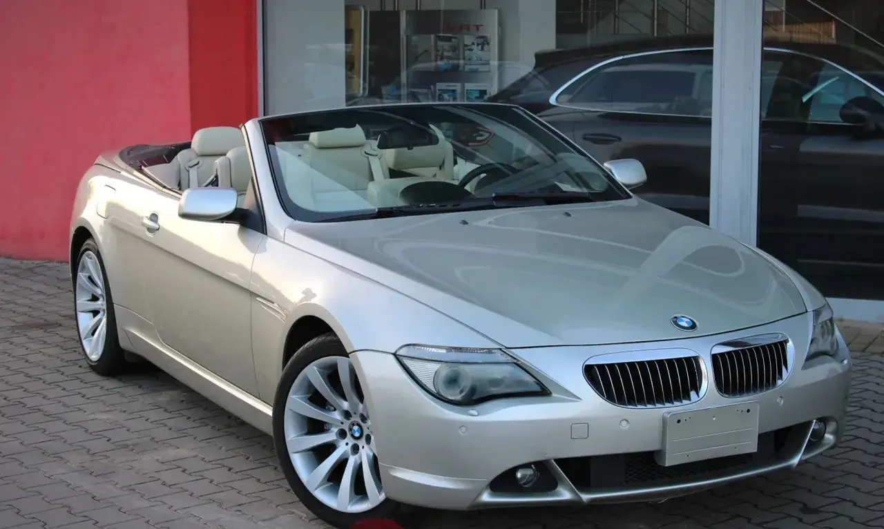 Srebrny kabriolet BMW E64 z beżowym wnętrzem stoi przed salonem samochodowym.