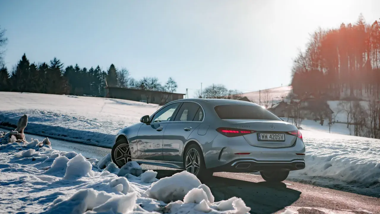 Srebrny Mercedes C 300 na tle ośnieżonych wzgórz i lasu. Zima nie straszna temu eleganckiemu autu.