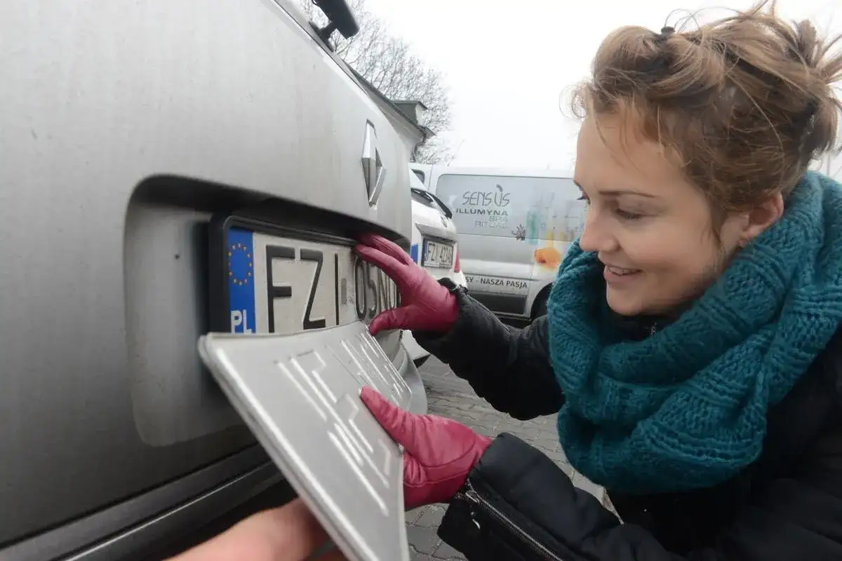 Kobieta w czerwonych rękawiczkach montuje tablicę rejestracyjną. To ważny etap lch rejestracja pojazdu.