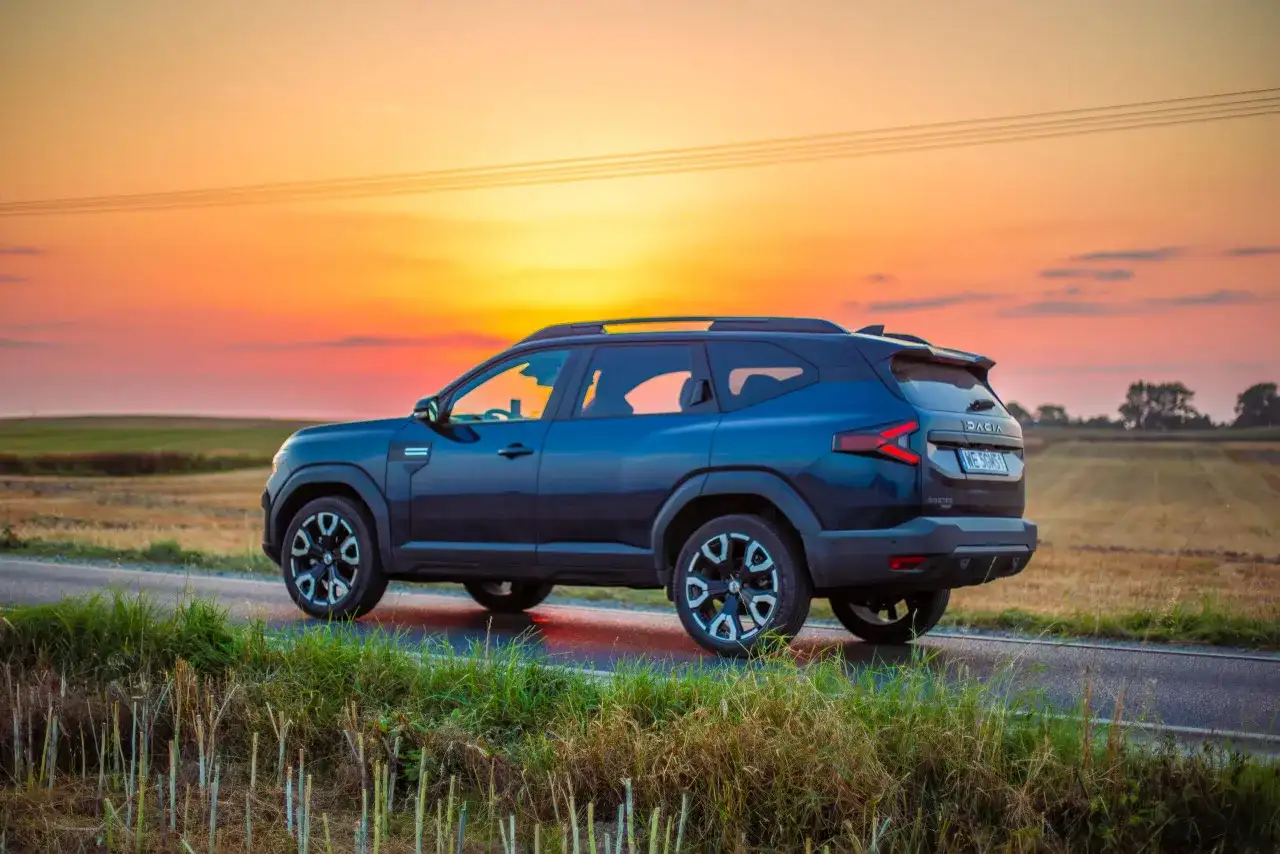 Ciemnoniebieska Dacia 4x4 na tle zachodzącego słońca, na polnej drodze.
