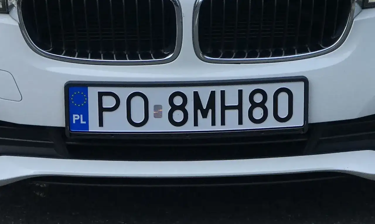 Biała maska samochodu z widocznym fragmentem kratki i tablicą rejestracyjną PO 8MH80.