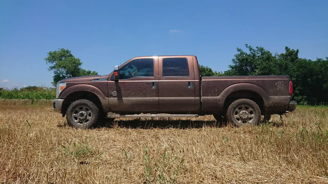 Brązowy Ford F250, ubrudzony ziemią, stoi na polu z suchą trawą.