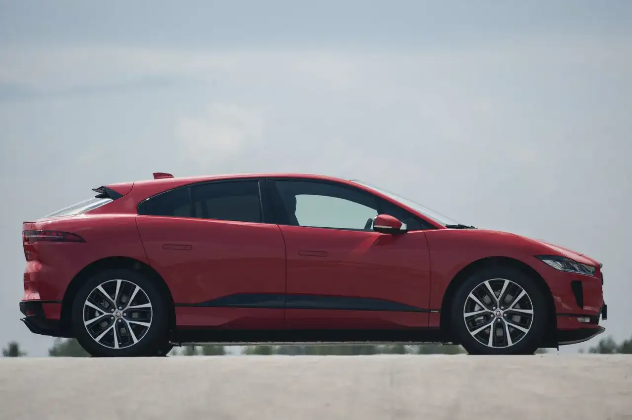 Czerwony jaguar elektryczny w profilu, z widokiem na jego aerodynamiczną sylwetkę i felgi.