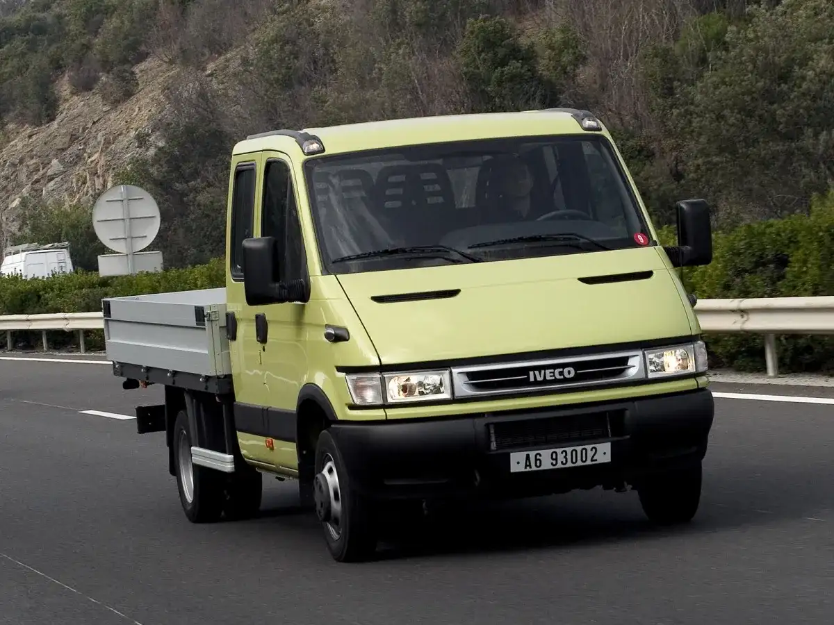 Żółty Iveco Daily 3 z podwójną kabiną i skrzynią ładunkową jedzie po drodze.