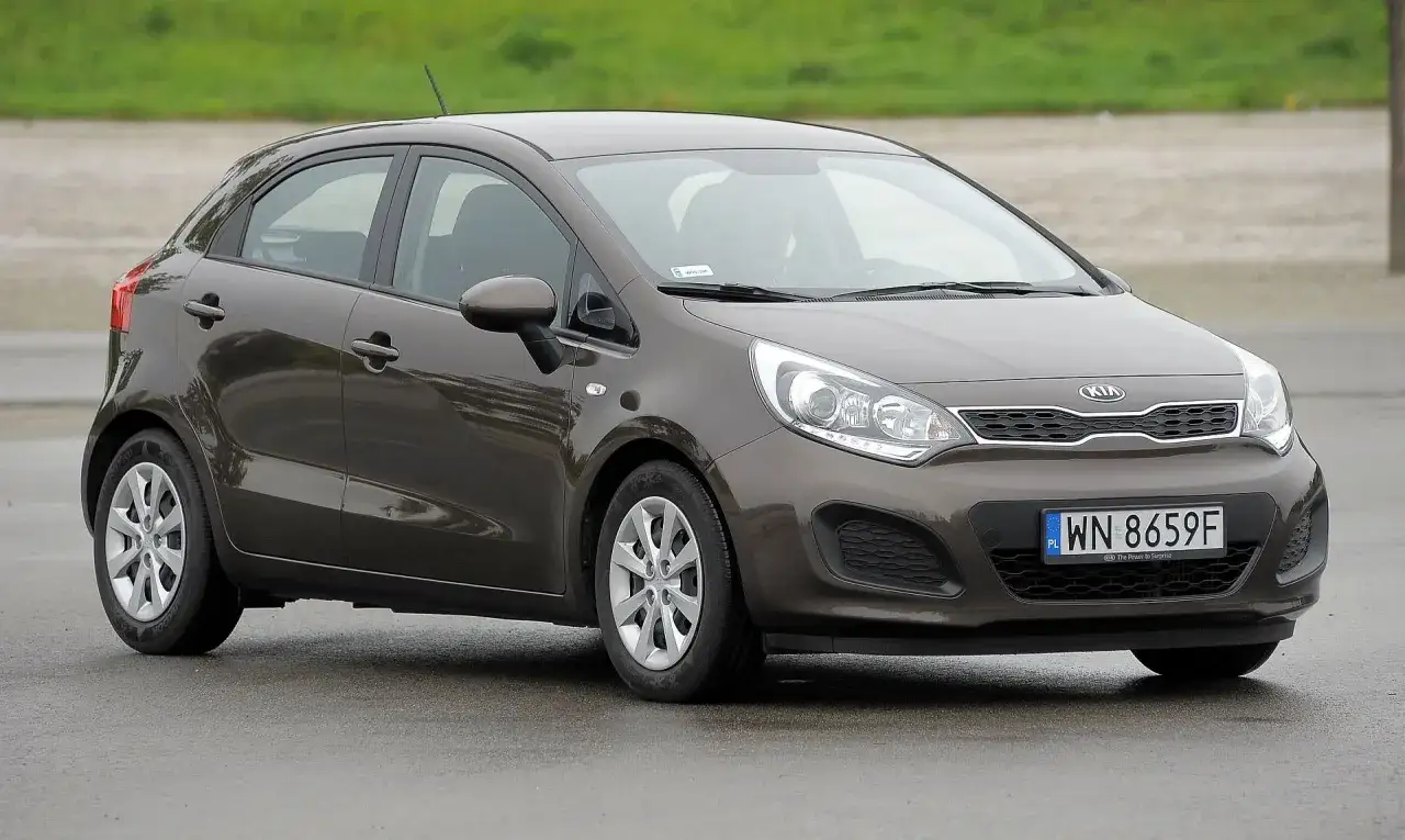 Brązowy Kia Rio na mokrej drodze. Wiele osób szuka kia rio opinie przed zakupem.