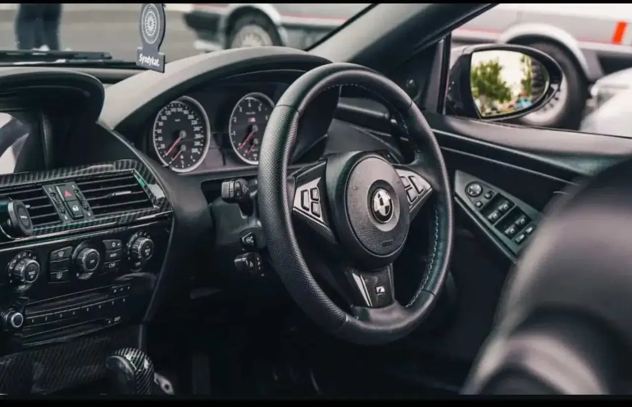 Wnętrze BMW E64 z czarną kierownicą, deską rozdzielczą i elementami z włókna węglowego.