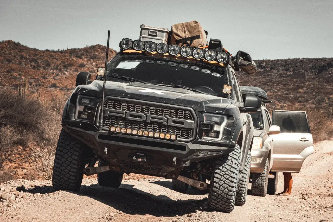 Czarny Ford F-150 Raptor z bagażem na dachu i dodatkowymi światłami, gotowy na pustynną wyprawę.
