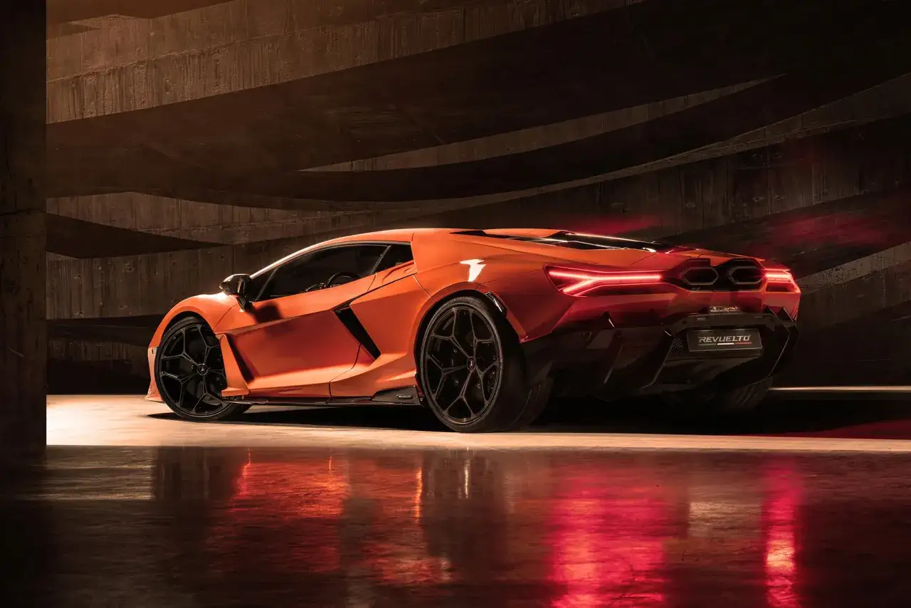 Pomarańczowy Lamborghini Revuelto z czarnymi felgami, stojący w betonowym garażu, odbijający się w mokrej podłodze.