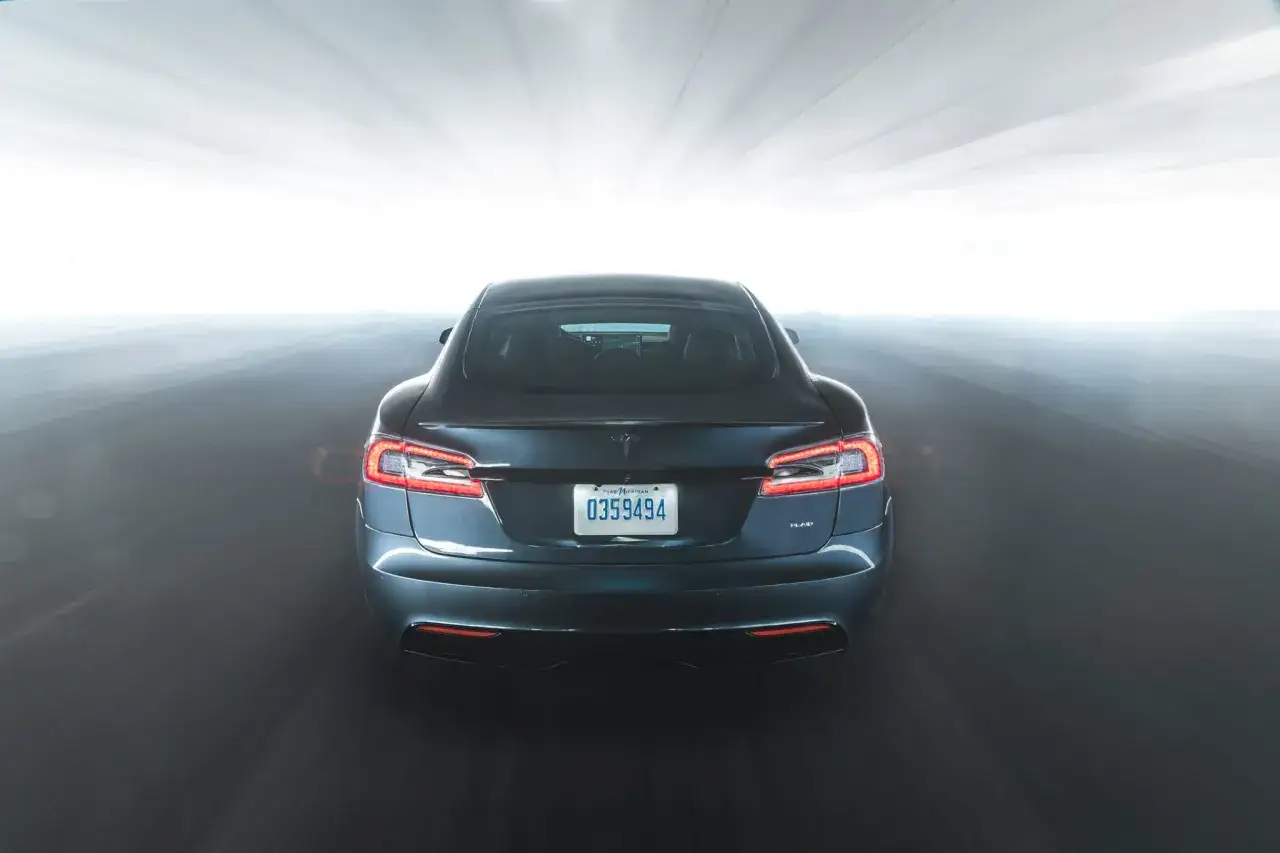 Tylna część Tesla Model S Plaid w ciemnym kolorze, pędząca przez tunel z rozmazanym światłem.