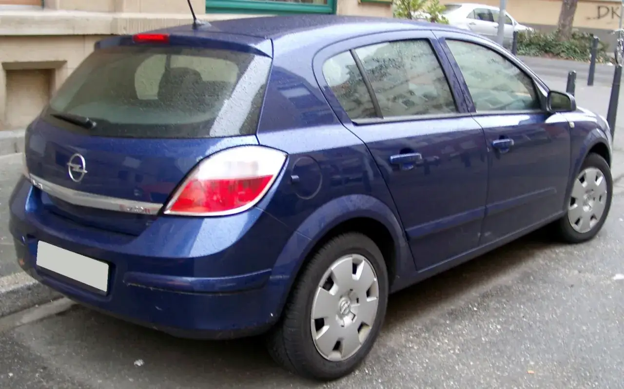 Granatowy Opel Astra 3 hatchback stoi na mokrej ulicy.
